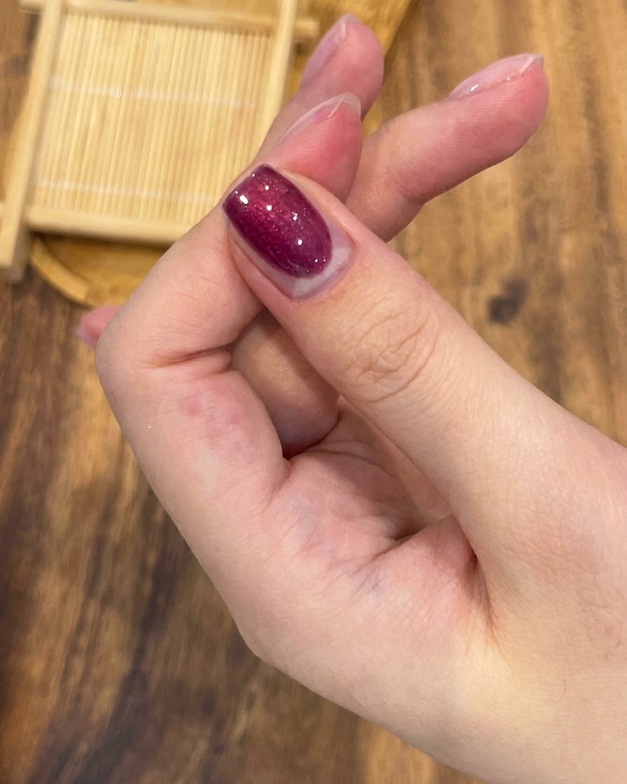 Un pincel de uñas profesional aplicando esmalte de gel magnético rojo rosa vibrante uniformemente a través de una uña.