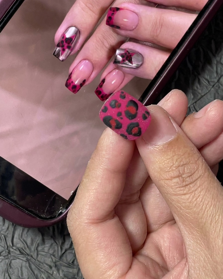 Una uña siendo pintada con esmalte de gel color rosa vibrante usando un pincel profesional.