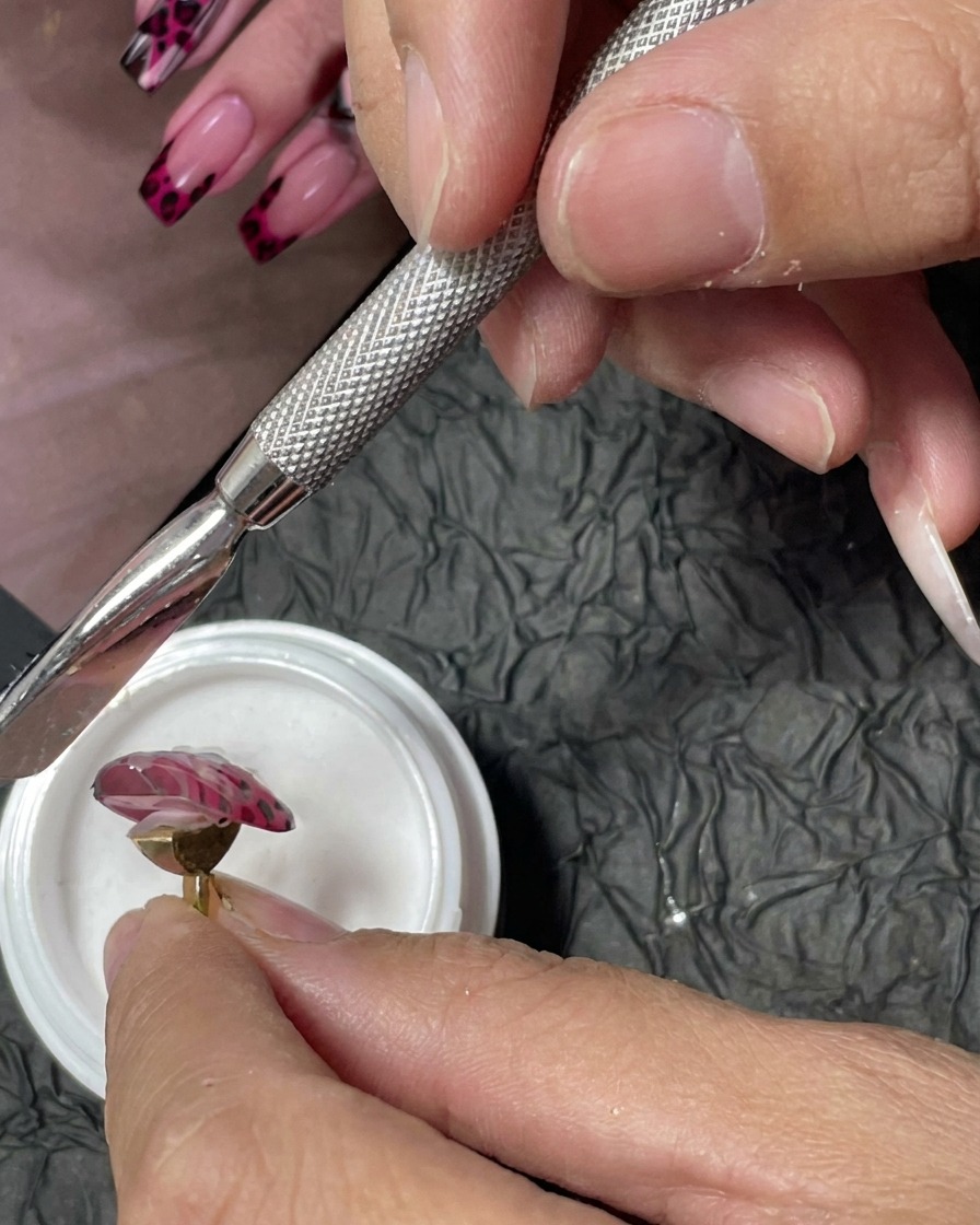 Herramienta de manicura esparciendo polvo acrílico blanco sobre puntos de gel rojo en una uña rosa.