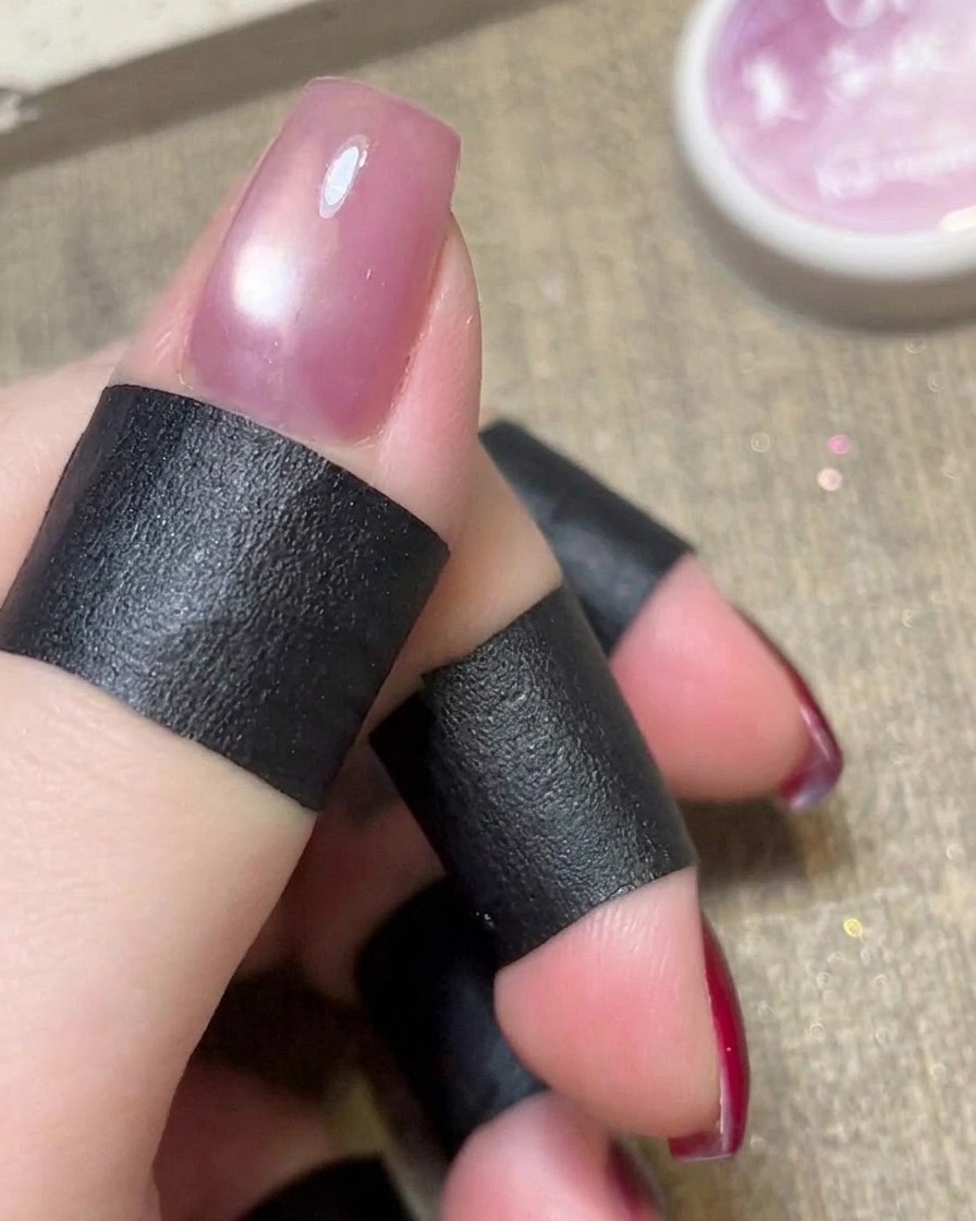 Un imán cilíndrico sostenido sobre el esmalte en gel cat eye rosa húmedo en una uña.