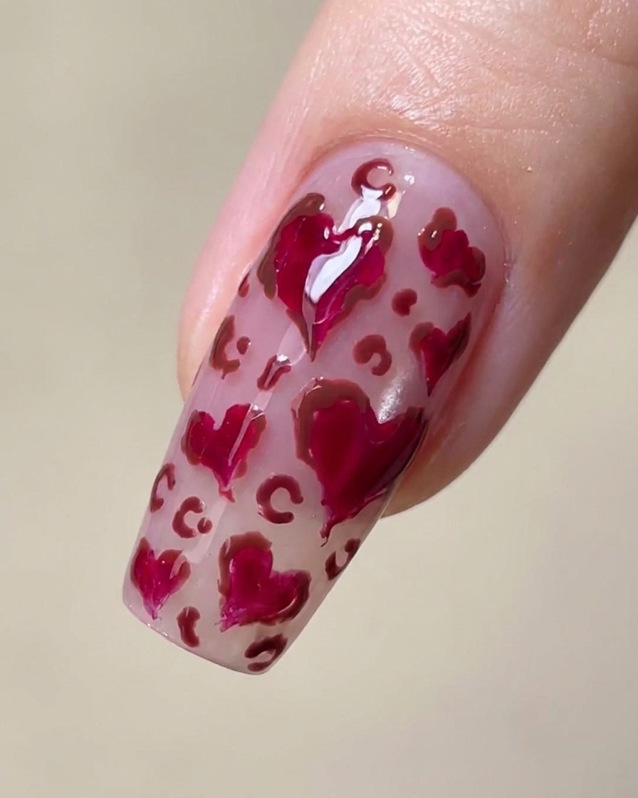 Primer plano de una uña con corazones magenta y delicadas manchas marrones de estampado de leopardo entre ellos.