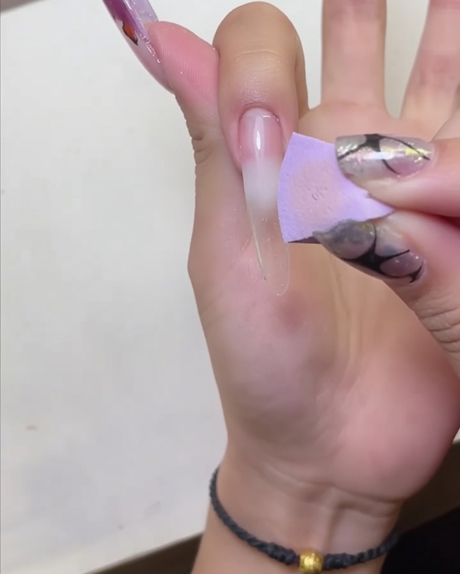 Una mano posicionada bajo una lámpara LED para curar el protector de cutículas aplicado.