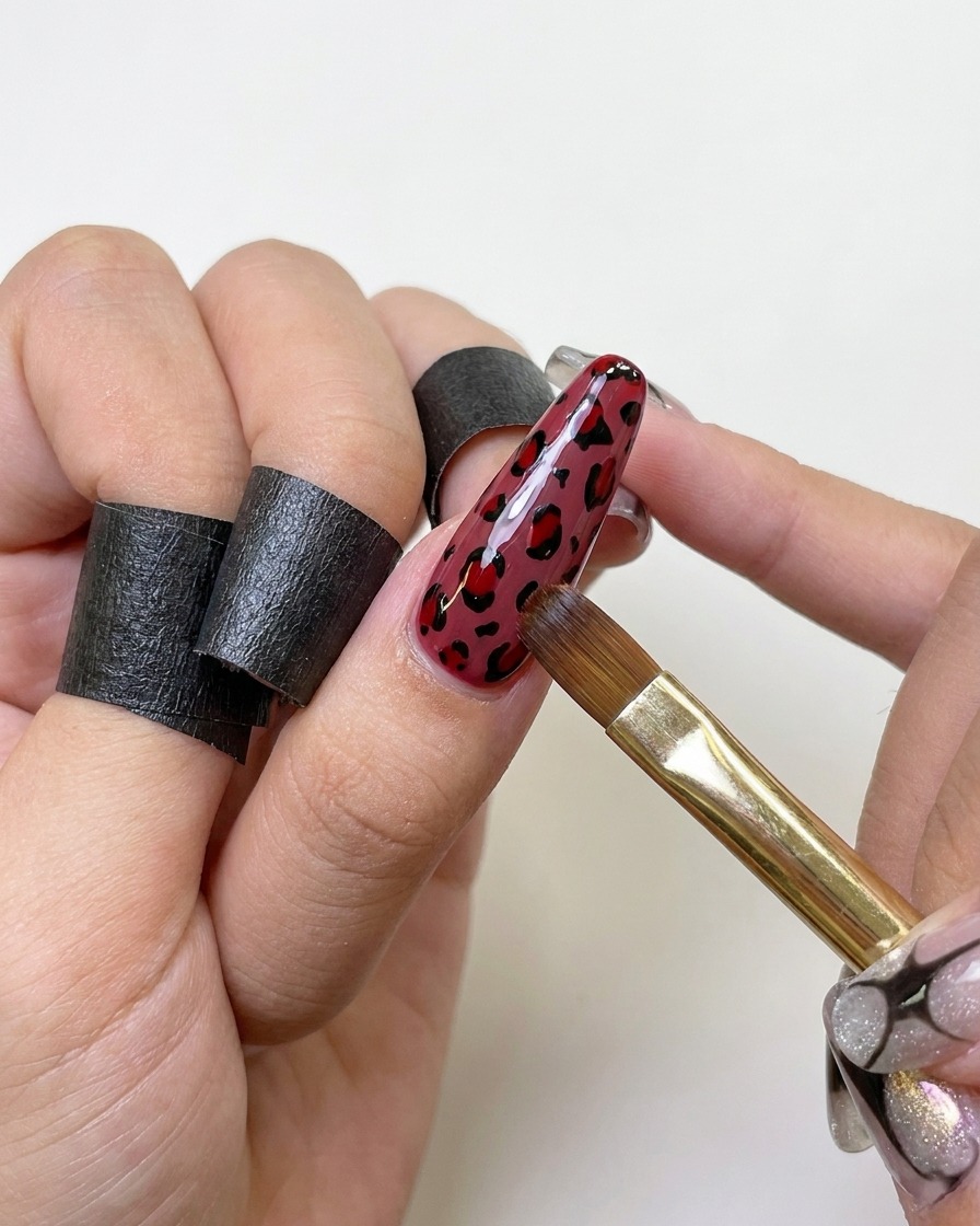 Un pincel de esmalte de gel aplicando una capa espesa de top coat transparente sobre una uña con diseño de leopardo.