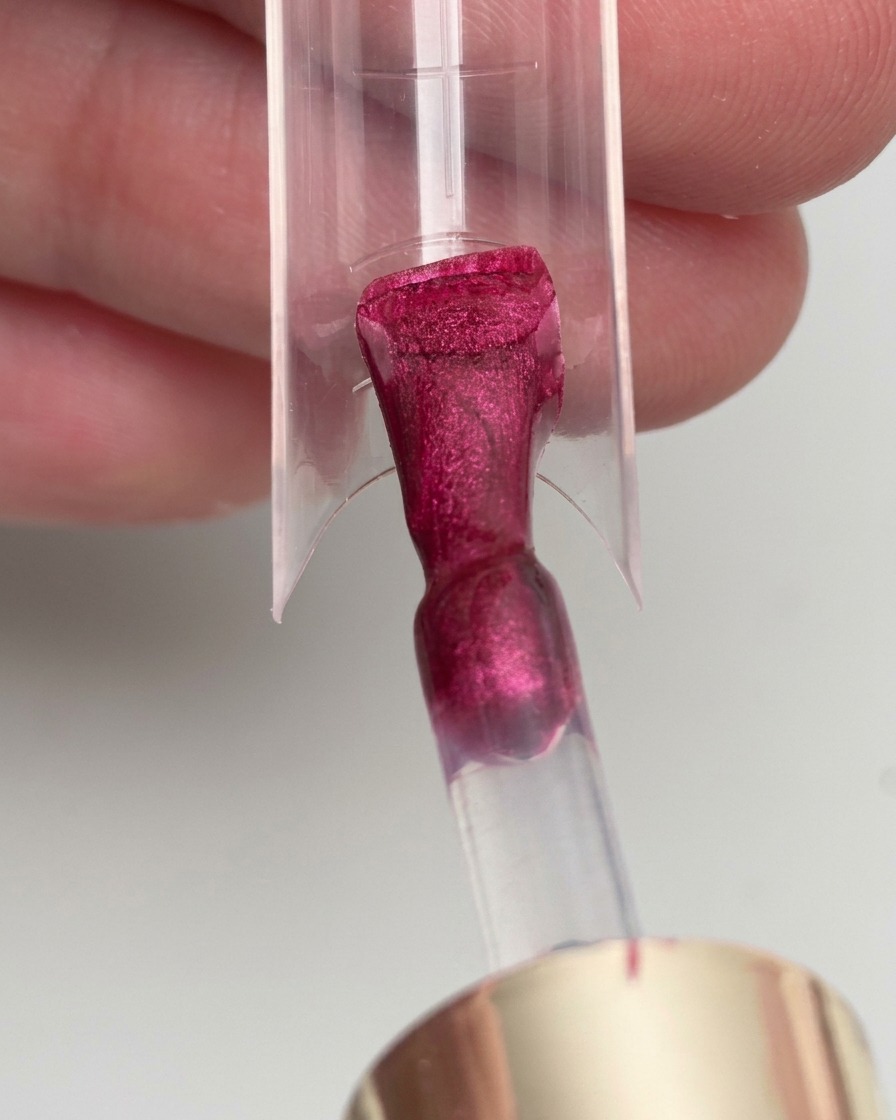 Un pincel aplicando esmalte en gel color magenta sobre una forma para extensión de uña.