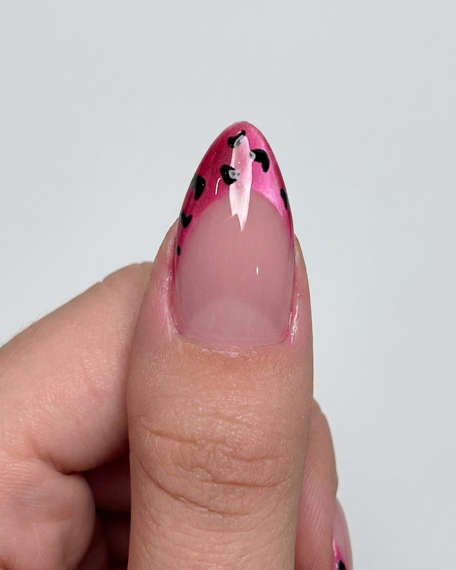 Un pincel liner añadiendo contornos negros delicados alrededor de los puntos en una punta francesa magenta.