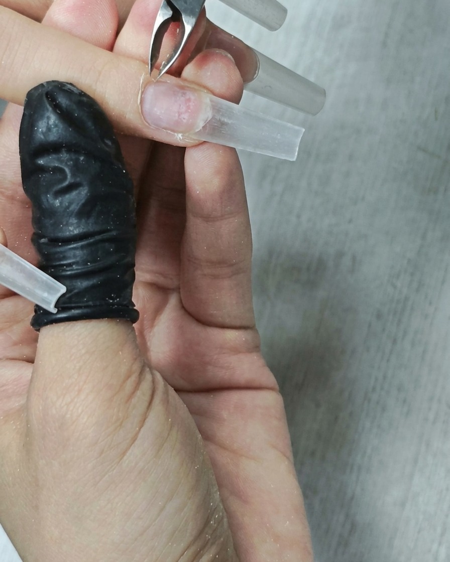 Una vista en primer plano de una broca de cutícula de metal utilizándose para limpiar alrededor del área de la cutícula de una uña.