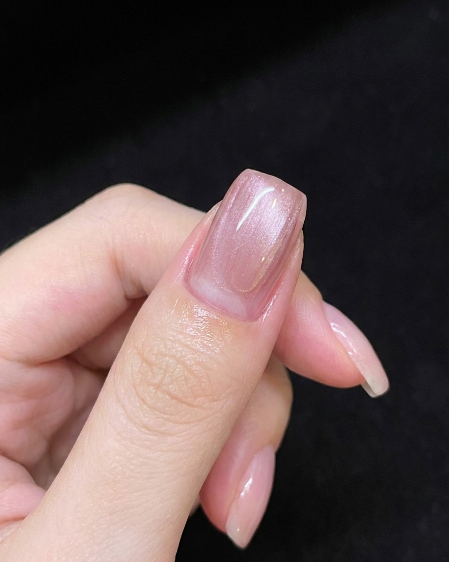 Una mano sosteniendo un imán sobre una uña cubierta con gel rosa para crear una línea de brillo diagonal.