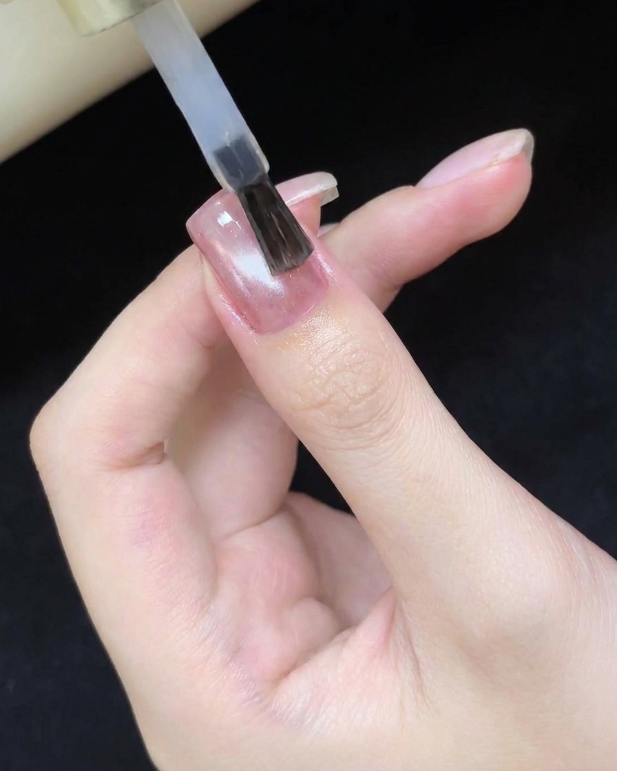 Un pincel aplicando un top coat transparente y brillante sobre el diseño de uñas ojo de gato ya curado.