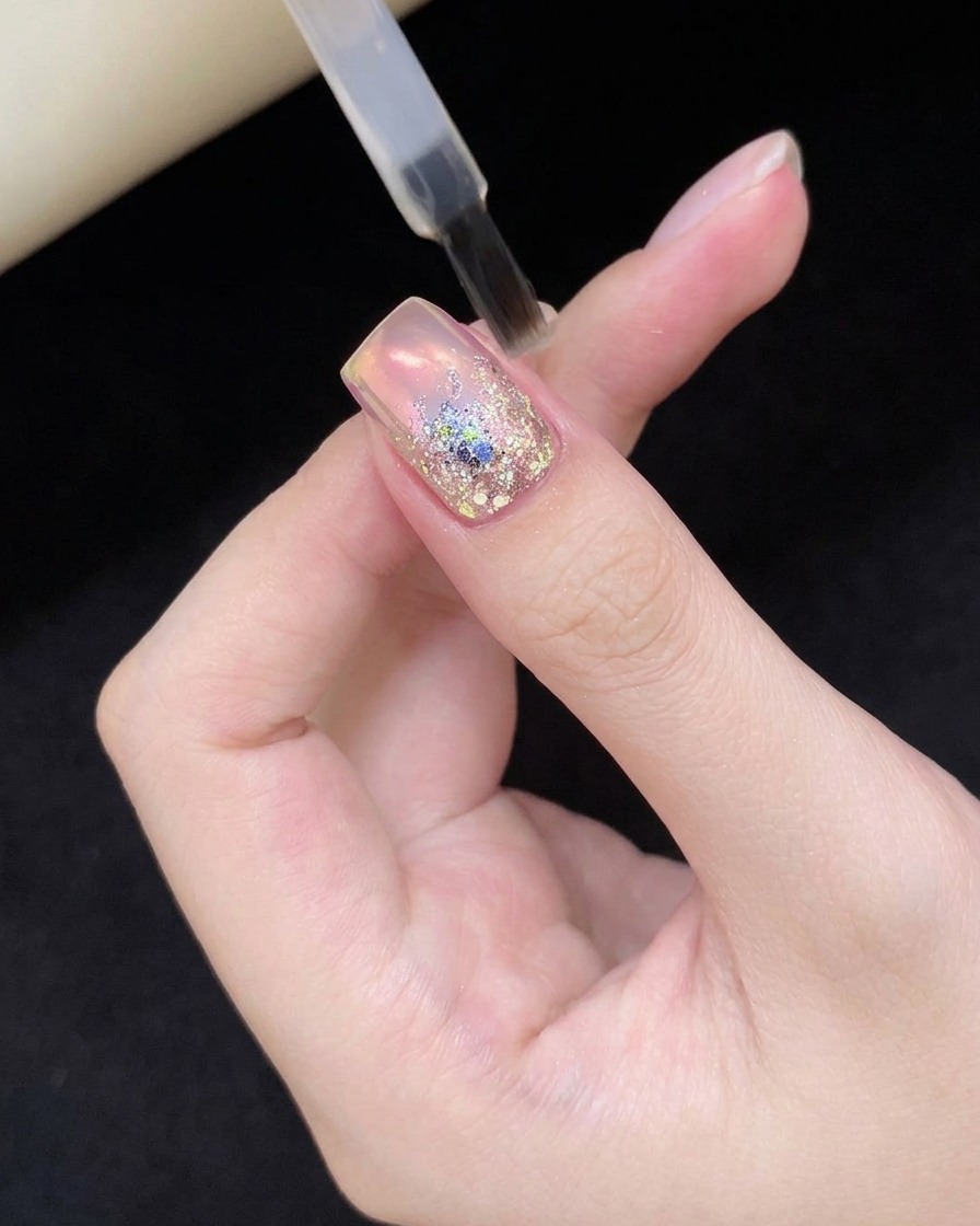 Una uña con nail art de glitter sostenida dentro de una lámpara profesional de curado UV/LED.