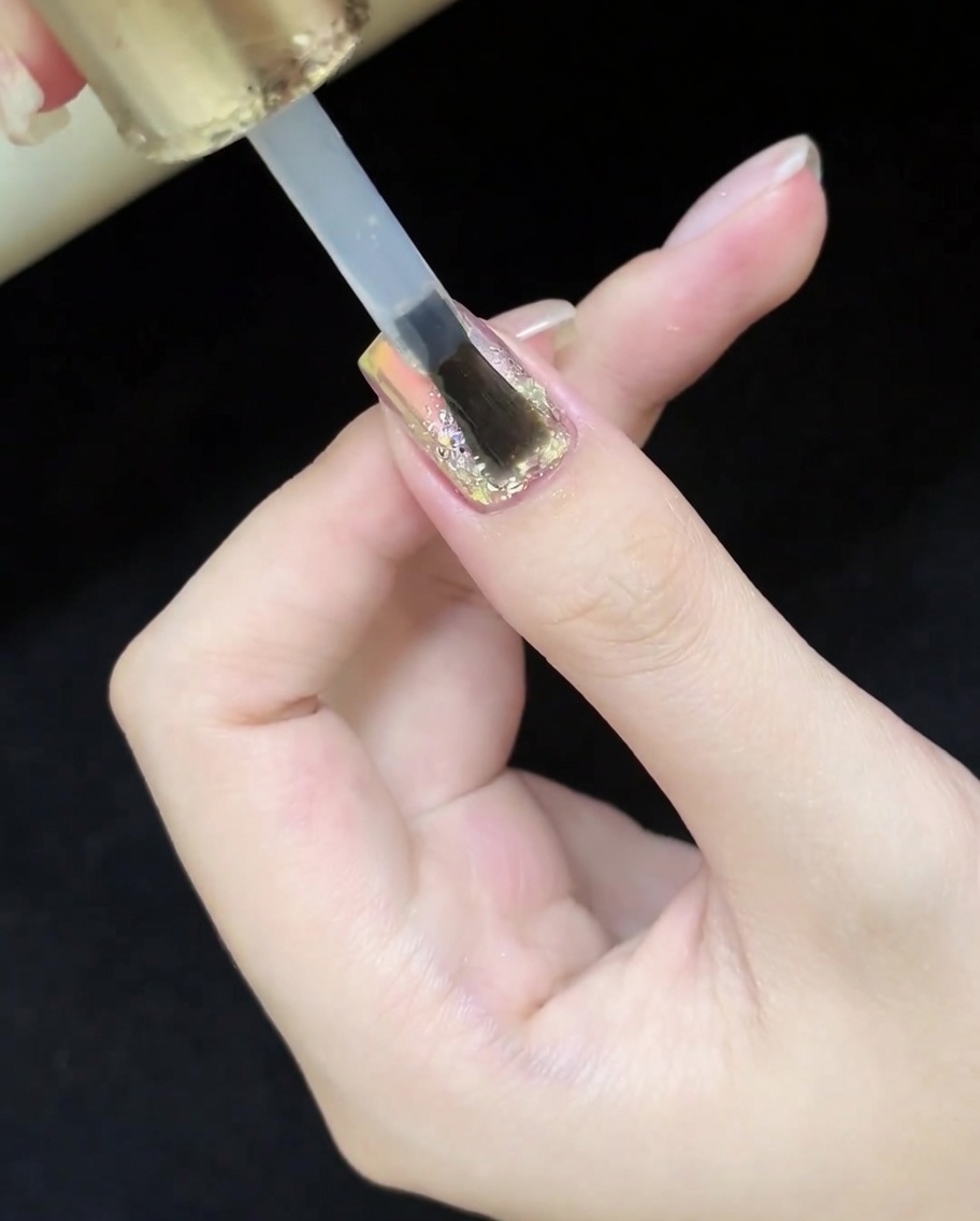 Un pincel aplicando un top coat transparente y brillante sobre el diseño terminado de uñas ojo de gato con glitter.