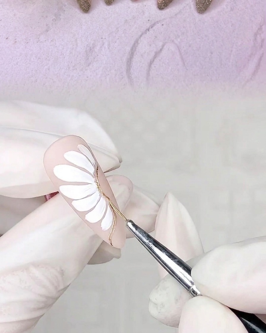 Una mano con una uña decorada colocada dentro de una lámpara UV para curar los contornos de gel adhesivo recién aplicados.