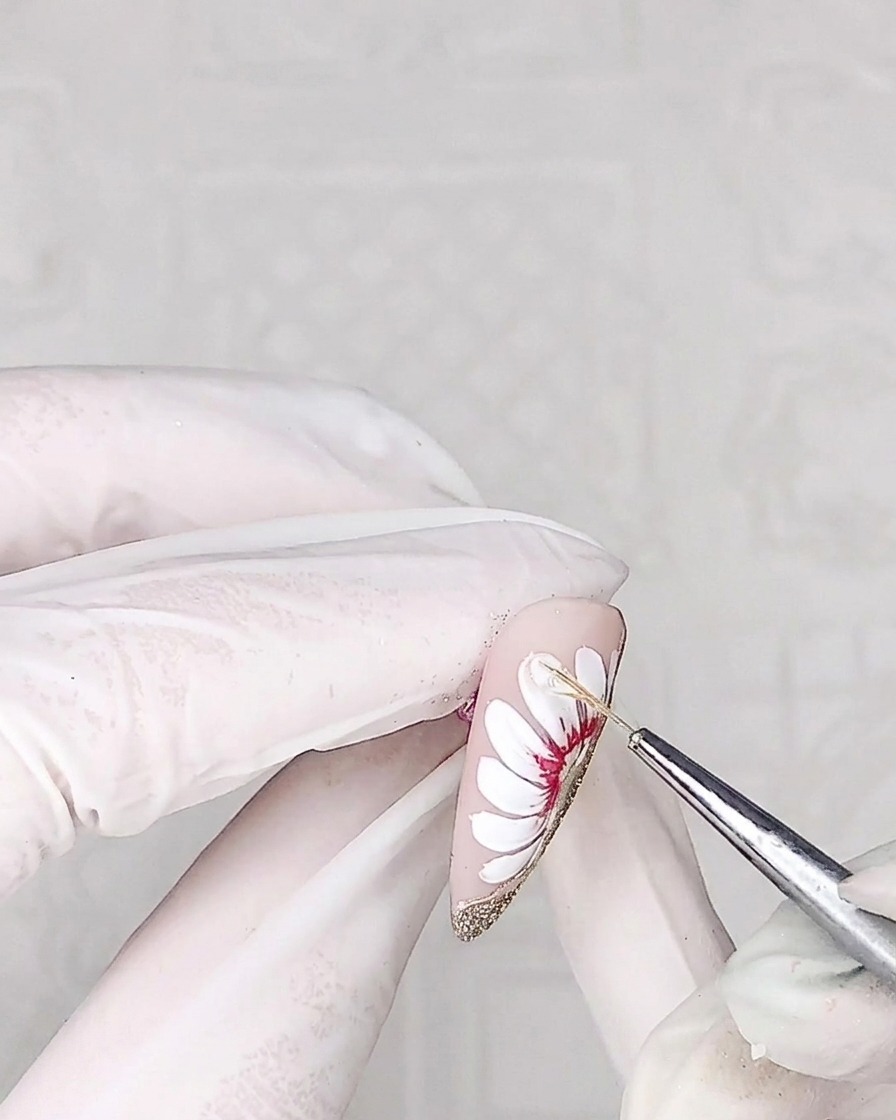 Primer plano de un pincel delineador aplicando un gel adhesivo espeso y transparente sobre la superficie de un pétalo de margarita.