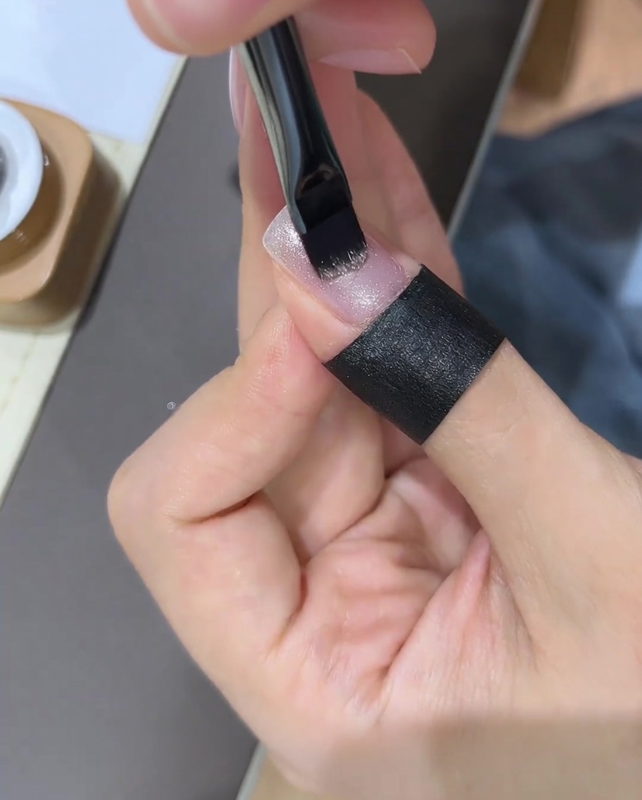 Una mano usando un imán de uñas sobre una uña de gel recién pintada para manipular las partículas de purpurina.
