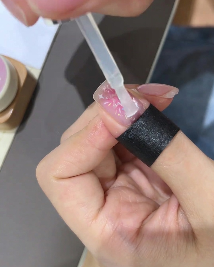 Un pincel aplicando una capa superior transparente sobre el diseño de uñas de estrellas completado.