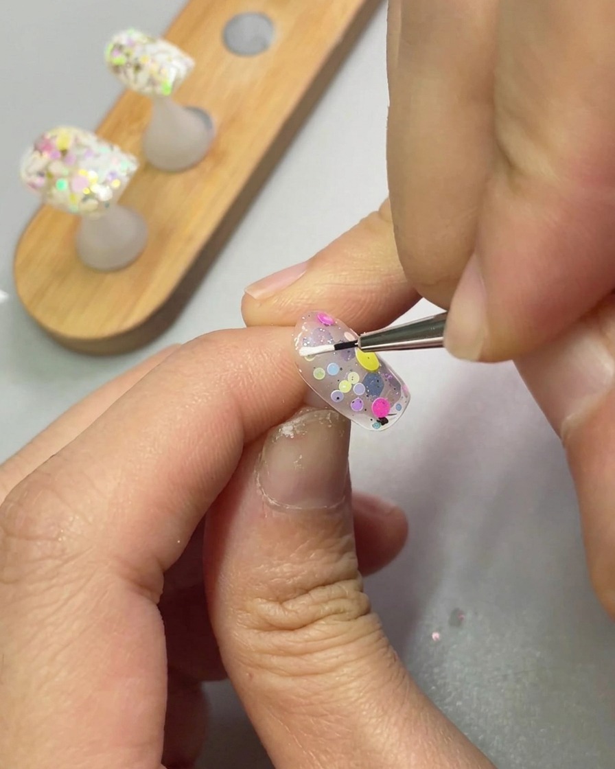 Un pincel de detalle fino aplicando gel de esculpido blanco para crear la forma de un pétalo en una uña.