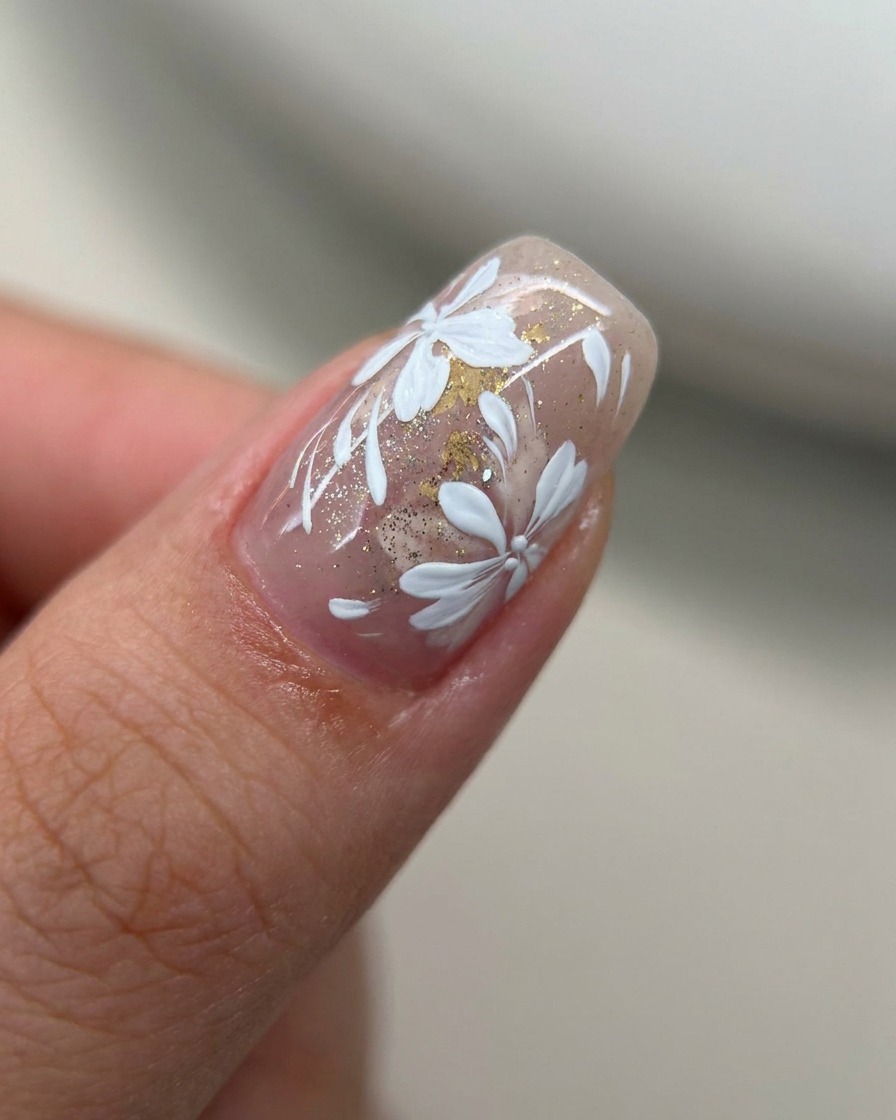 Primer plano de una uña con un tinte rosa nude traslúcido siendo cubierto con una capa fina de glitter dorado usando un pincel de gel.