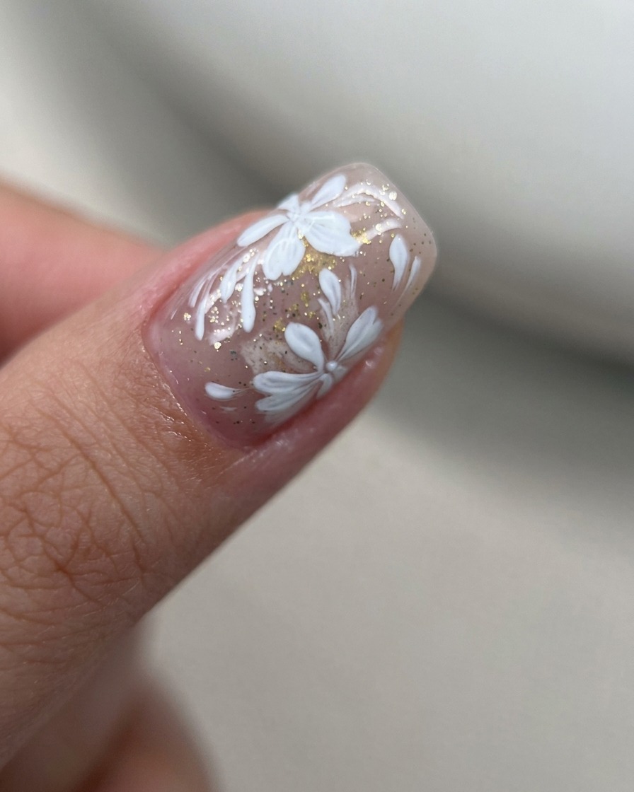 Una toma macro de pétalos de flores de gel blanco pintados en un grupo denso y concentrado sobre una uña nude.