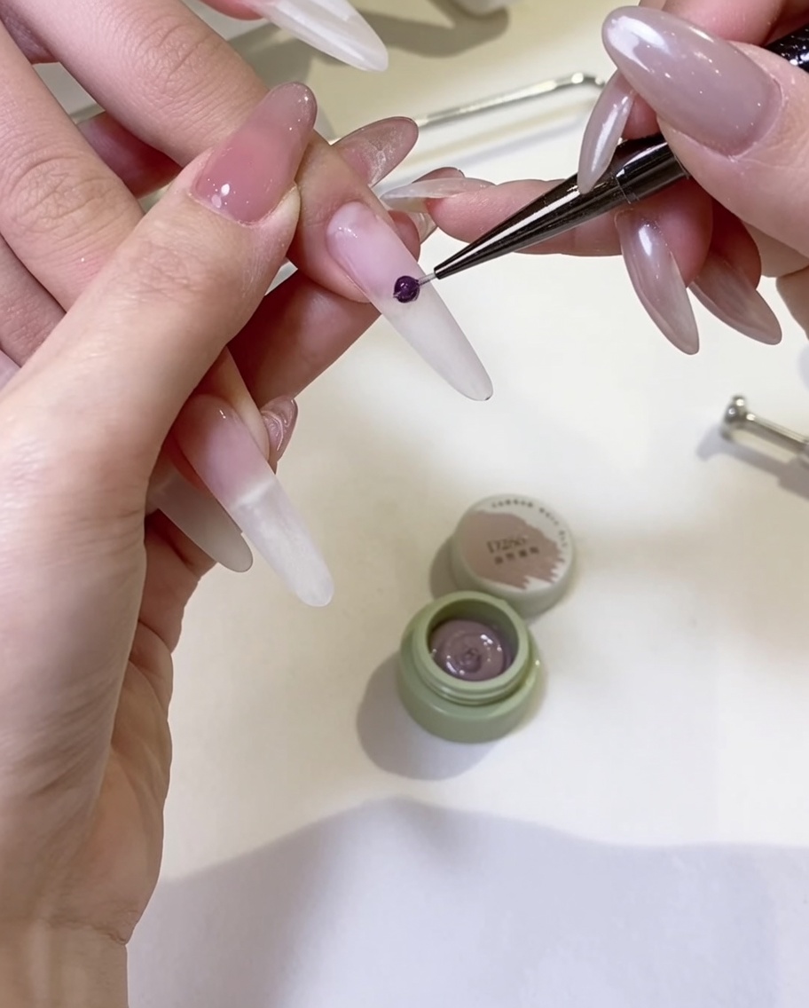 Un pincel de gel aplicando una capa suave de esmalte nude sobre la superficie de la uña.