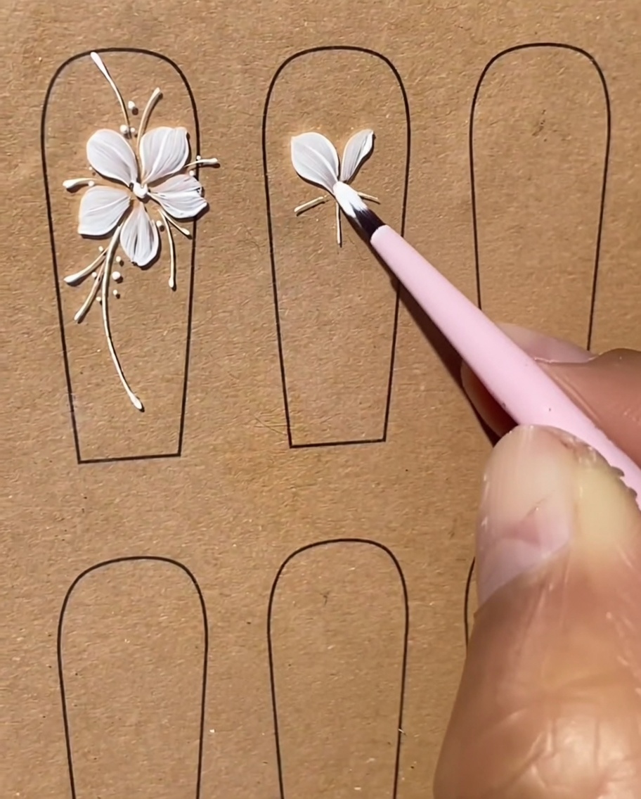 Un pincel dando forma cuidadosamente a un tercer pétalo de gel blanco como parte del diseño de la flor de cinco pétalos.