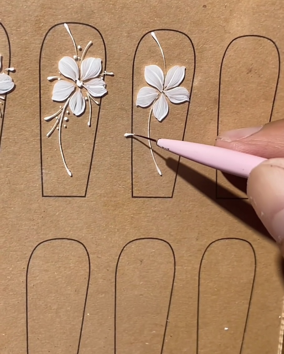 Primer plano que muestra un pincel liner añadiendo líneas blancas largas y delicadas entre los pétalos de una flor pintada.