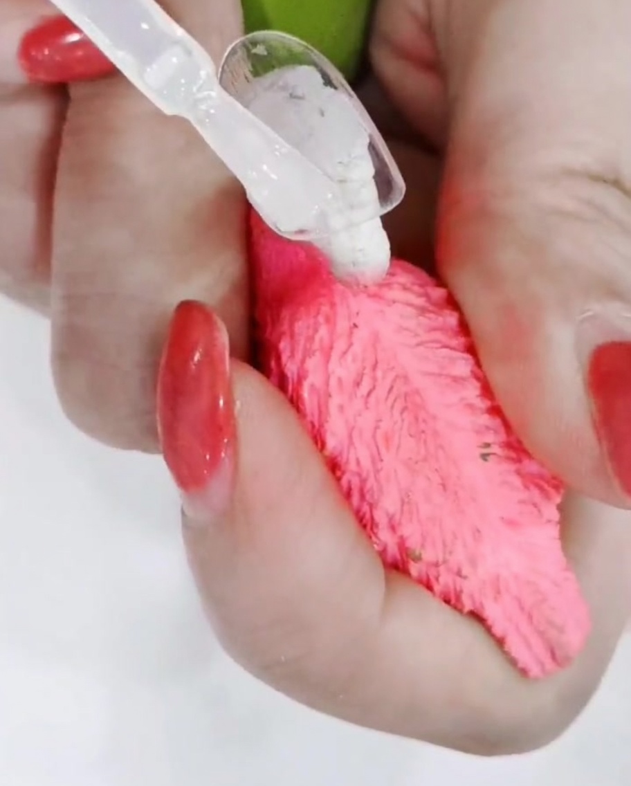 Un primer plano de un pincel de uñas perfilando con precisión los bordes de una margarita pintada a mano sobre una superficie de uña mate.