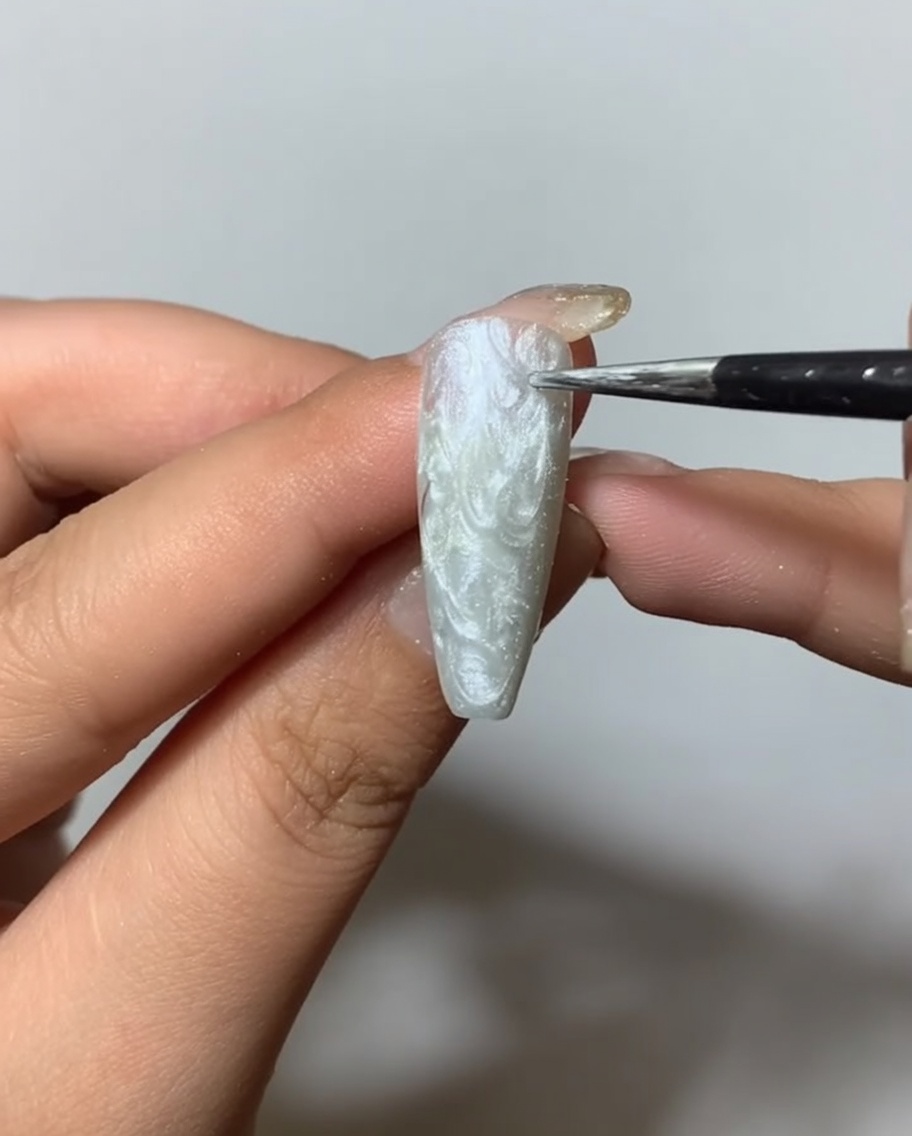 Un pincel aplicando un top coat mate transparente sobre una superficie de uña con spider gel plateado texturizado.