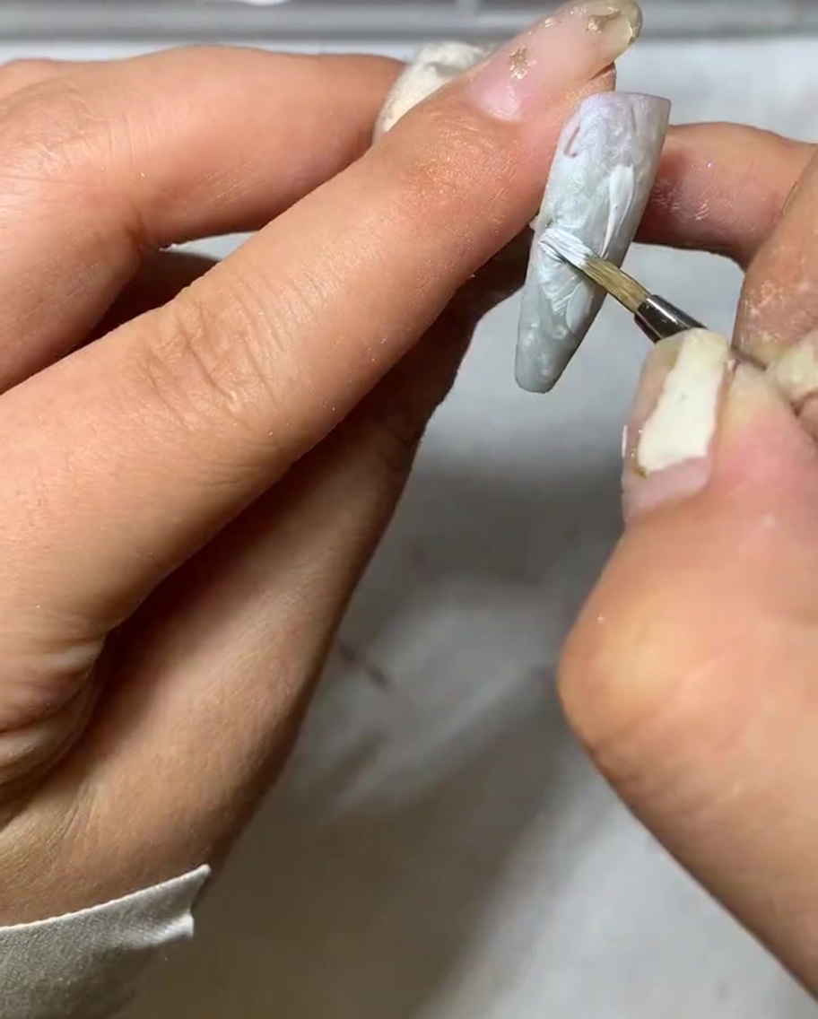 Una toma de detalle que muestra la punta de un pincel liner adelgazando el extremo de un pétalo de margarita blanco.