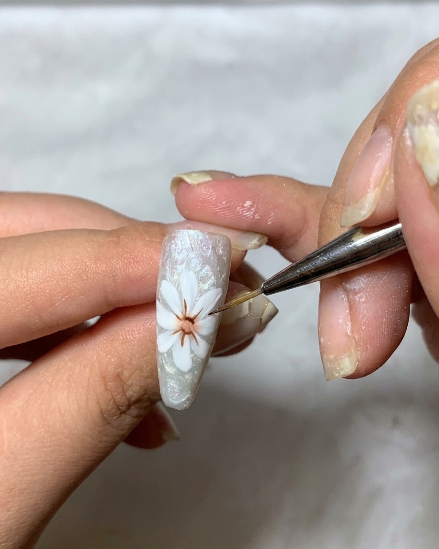 Un pincel fino aplicando un gel transparente espeso sobre el diseño de pétalos blancos en la uña para construir dimensión.
