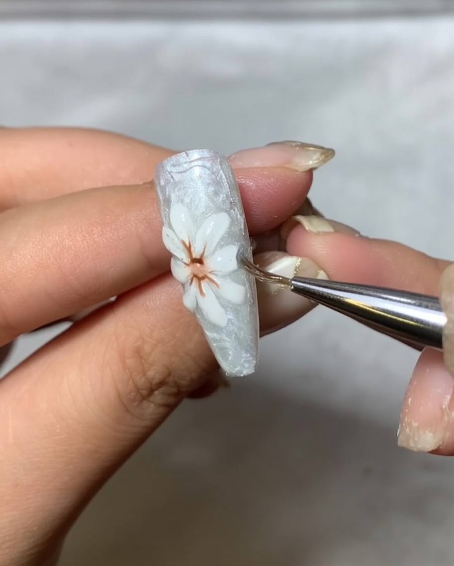 Un pincel aplicador puliendo suavemente polvo de espejo metálico sobre los pétalos blancos elevados del arte de uñas.