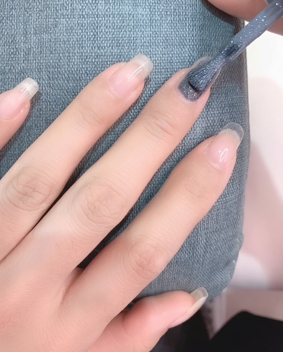 Vista de cerca de un pincel aplicando esmalte de gel gris claro sobre una uña limpia.