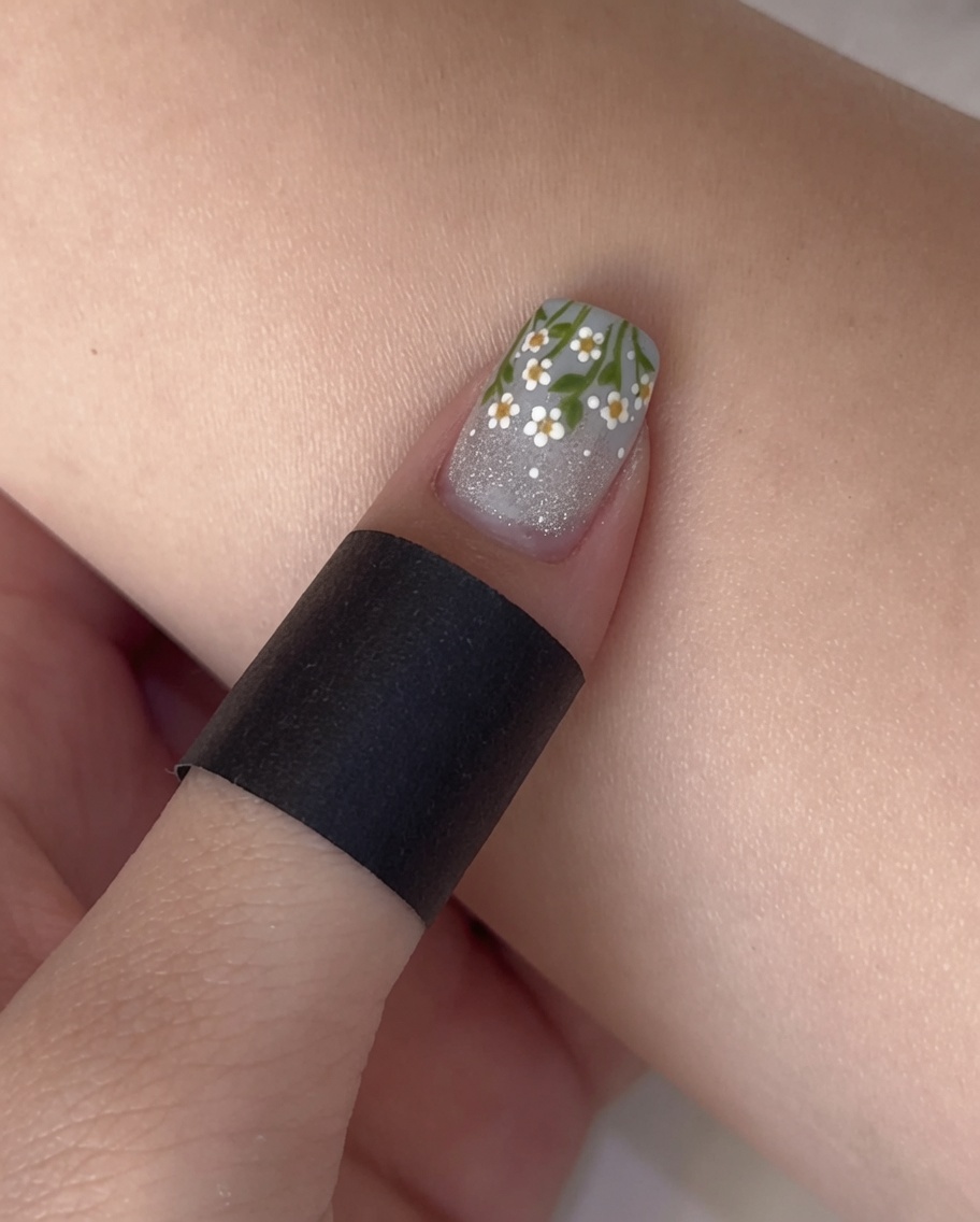 Un pincel de esmalte aplicando un top coat mate transparente sobre una uña con base brillante y punta francesa.