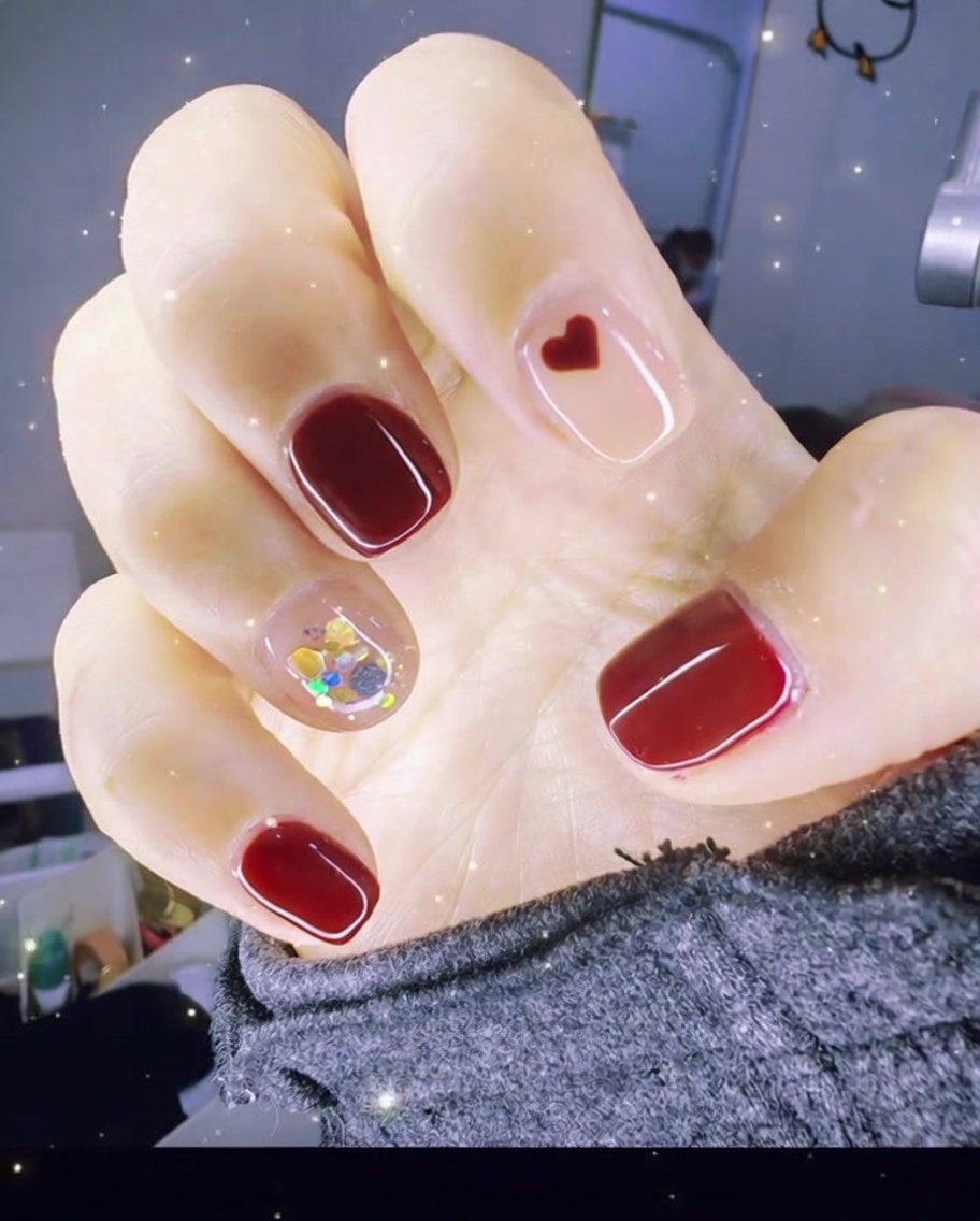 Pinzas colocando un pequeño charm de corazón rojo sobre la superficie de una uña con gel transparente.