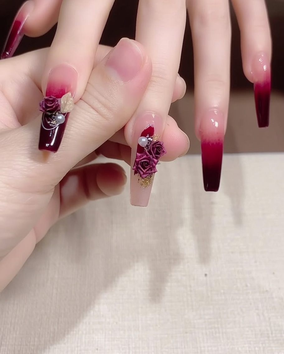 Pinzas colocando una perla pequeña y un dije metálico dorado junto a una rosa en una uña.