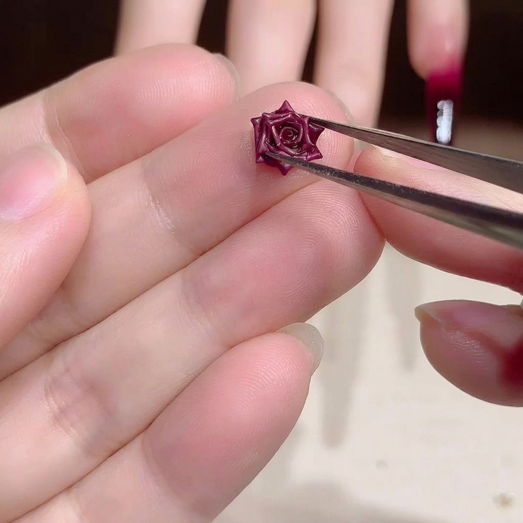 Primer plano de unas pinzas metálicas sosteniendo un pequeño y detallado dije de rosa seca roja.