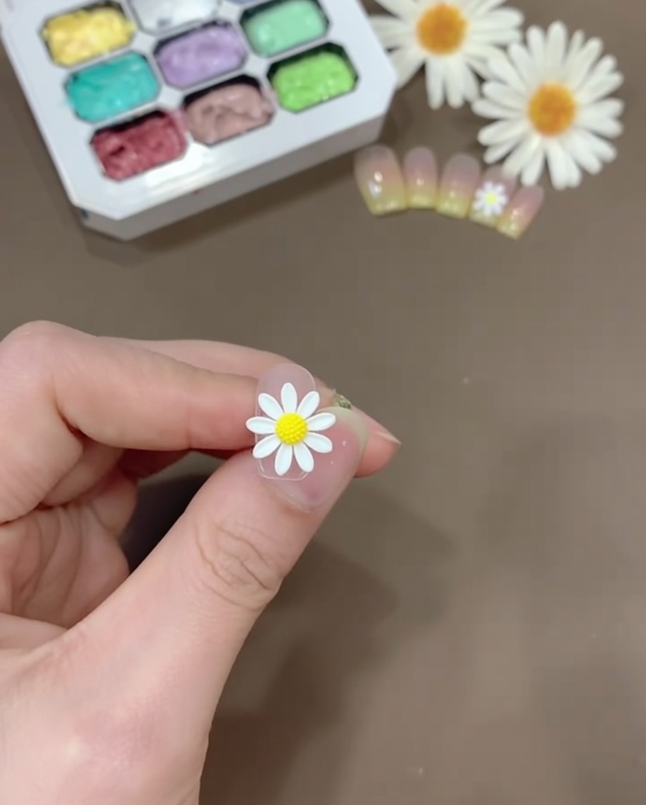 Una pequeña cantidad de gel amarillo mezclado con base coat transparente sobre una paleta de plástico.