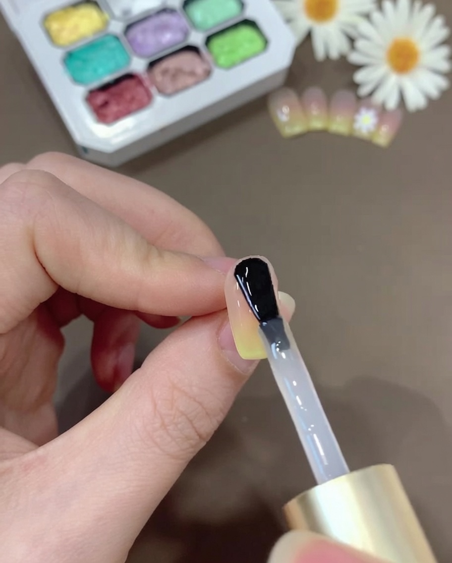 Un pincel aplicando una capa de top coat transparente sobre la uña degradada para dar un acabado brillante.
