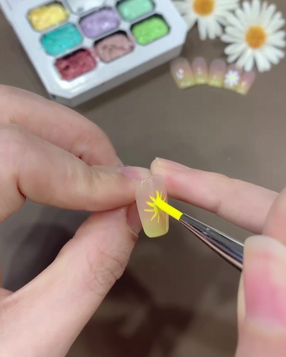 Un pincel para nail art aplicando gel blanco para formar pétalos redondeados de margarita sobre las guías previamente marcadas.