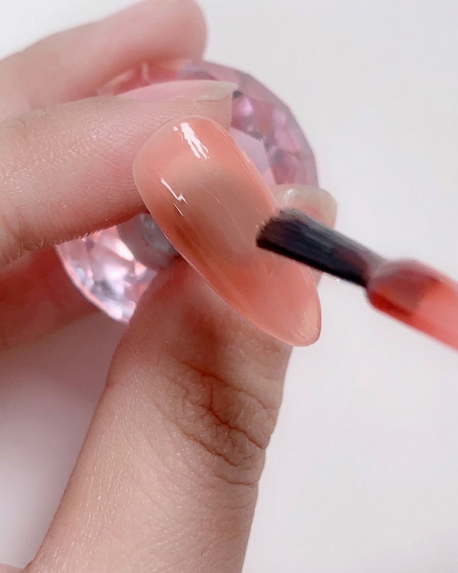 Un pincel aplicando una capa de esmalte en gel rosa suave en el centro de la uña.
