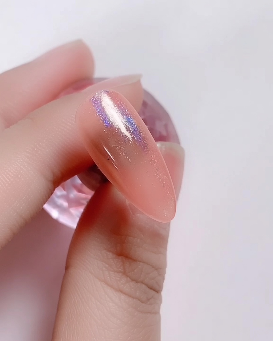 Un pequeño aplicador de esponja frotando polvo láser iridiscente sobre la uña de gel rosa.