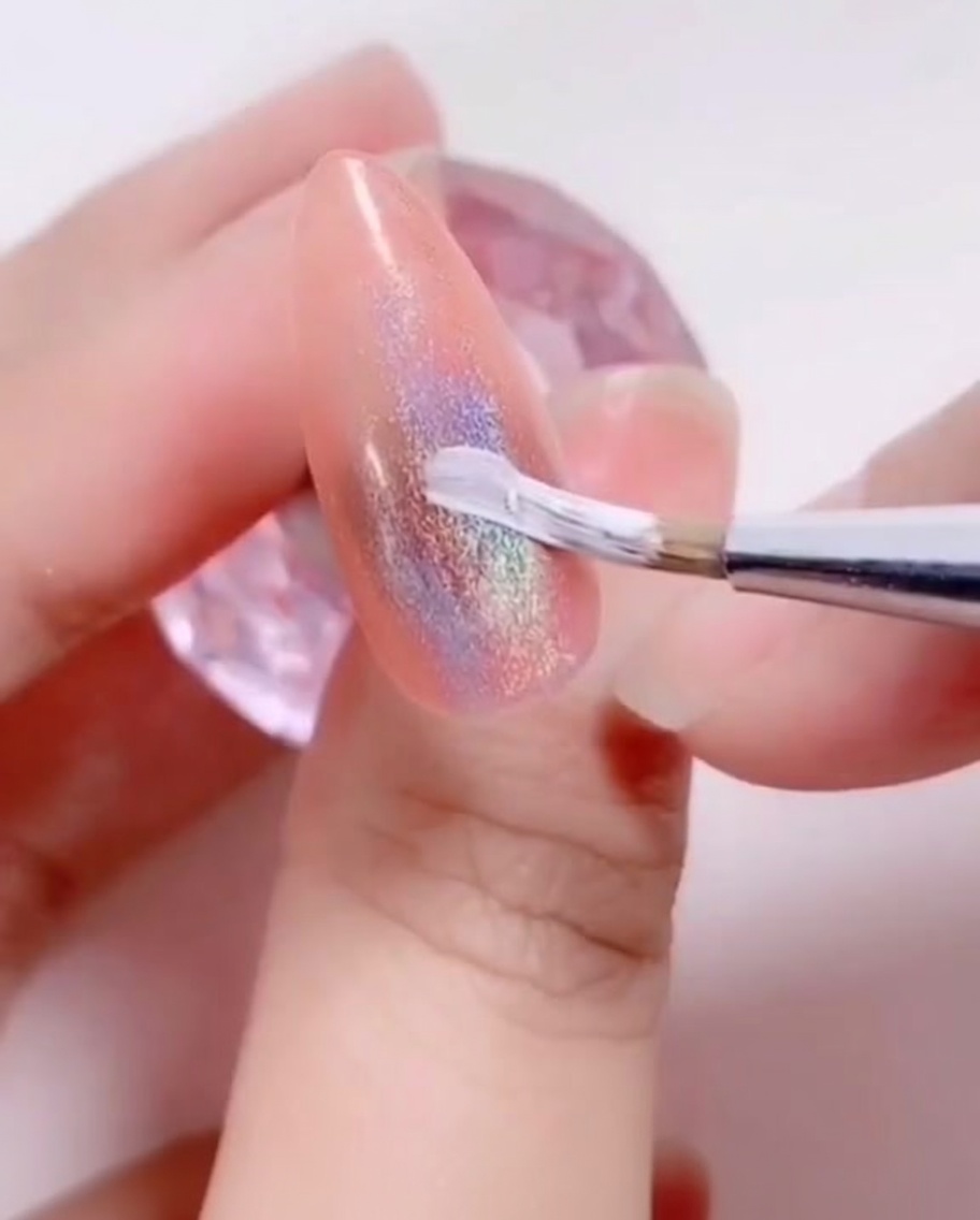 Un pincel delineador fino aplicando un diseño de pétalos de gel blanco sobre la superficie de la uña.