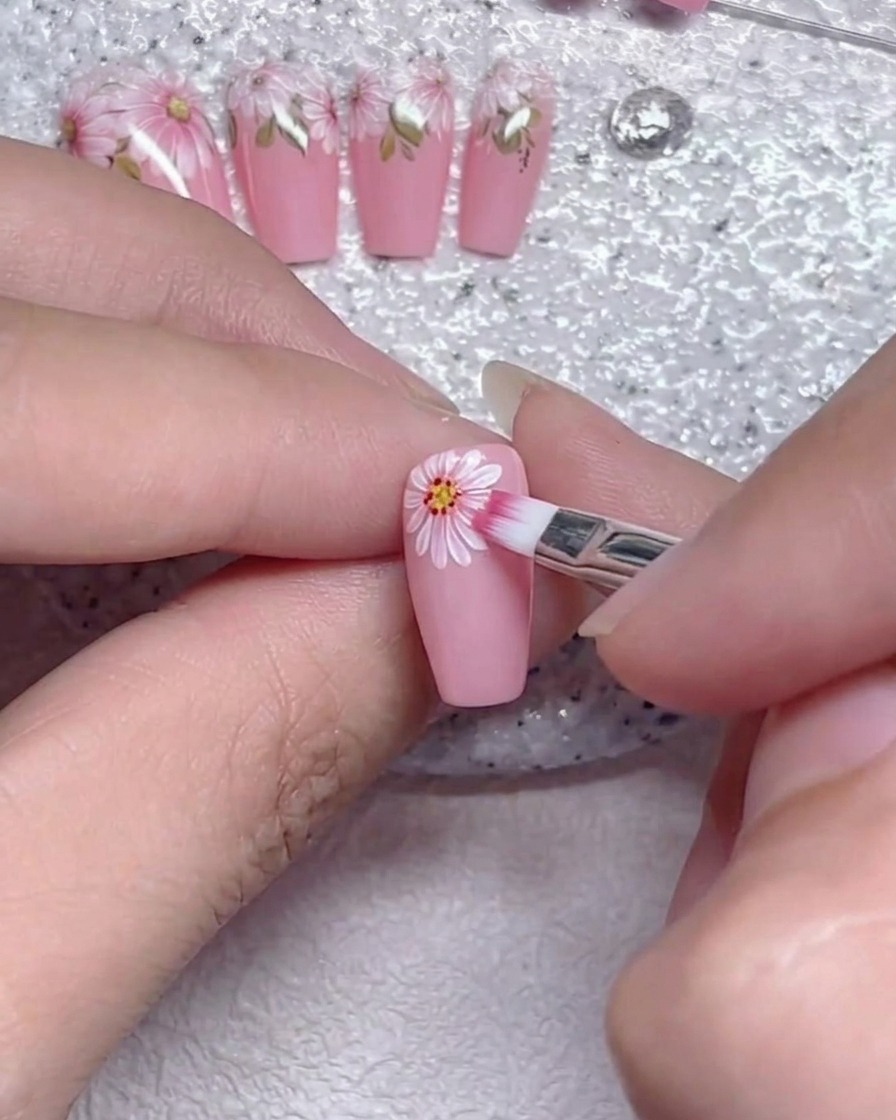Un pincel plano difuminando suavemente los bordes de los pétalos de la flor blanca sobre una uña rosa.