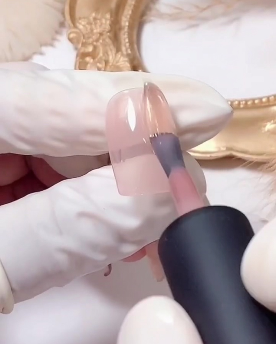 Un pincel plano depositando gel de purpurina plateada en la punta de una uña con base rosa.