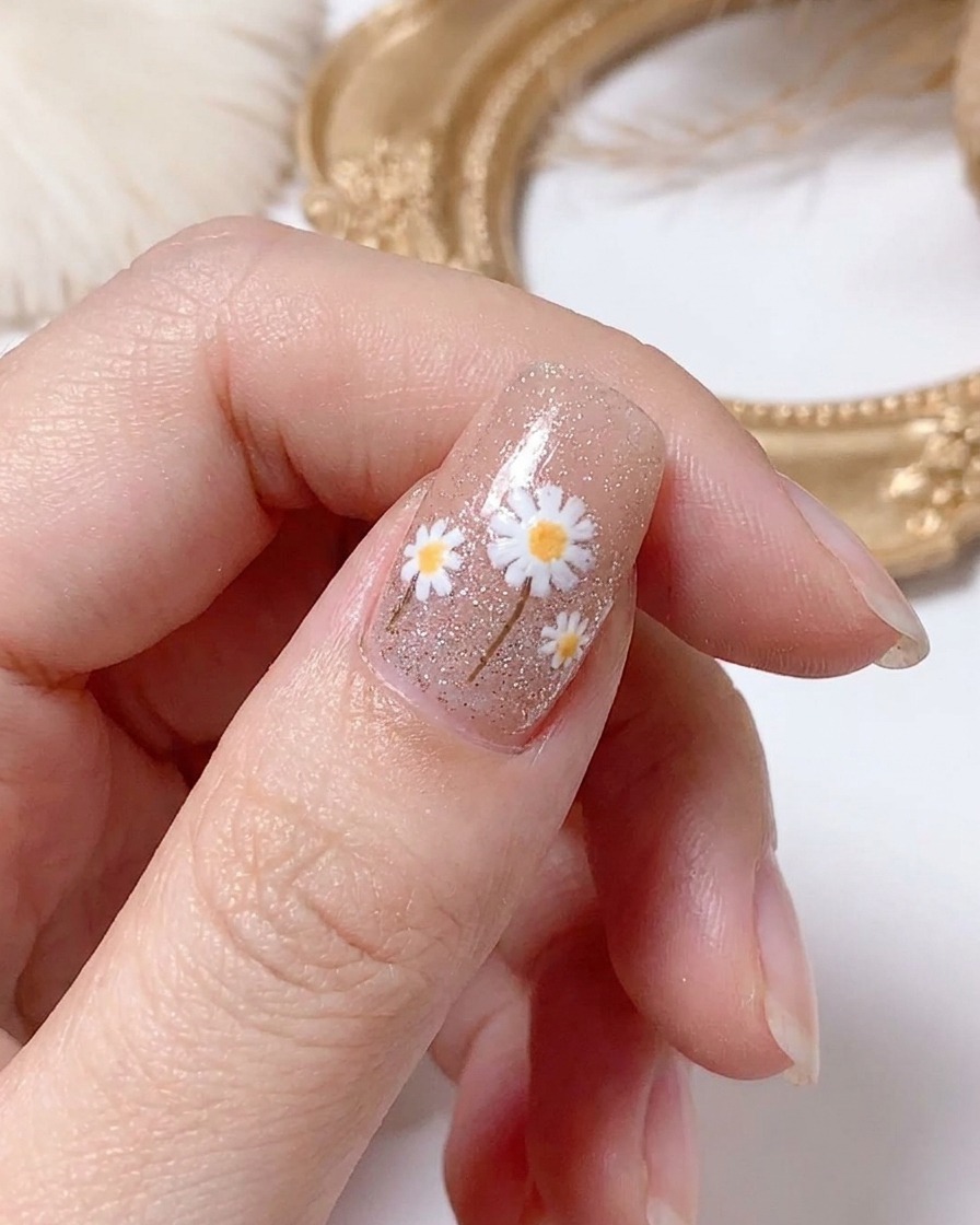 Una mano curando el diseño de uñas de margarita terminado bajo una lámpara.