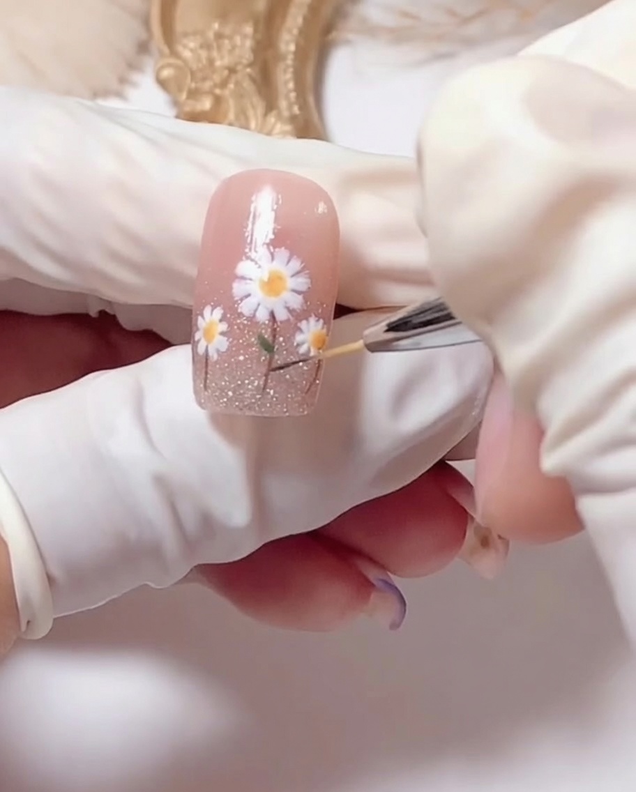 Un pincel aplicando top coat transparente y brillante sobre el diseño de uñas de margarita terminado.