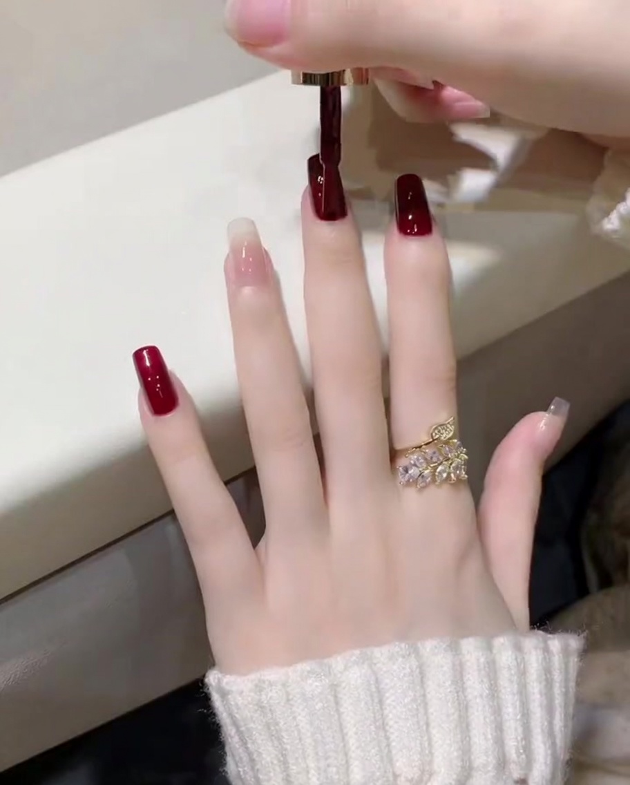Primer plano de un esmalte de gel rojo vino aplicado con un pincel en la uña del pulgar.