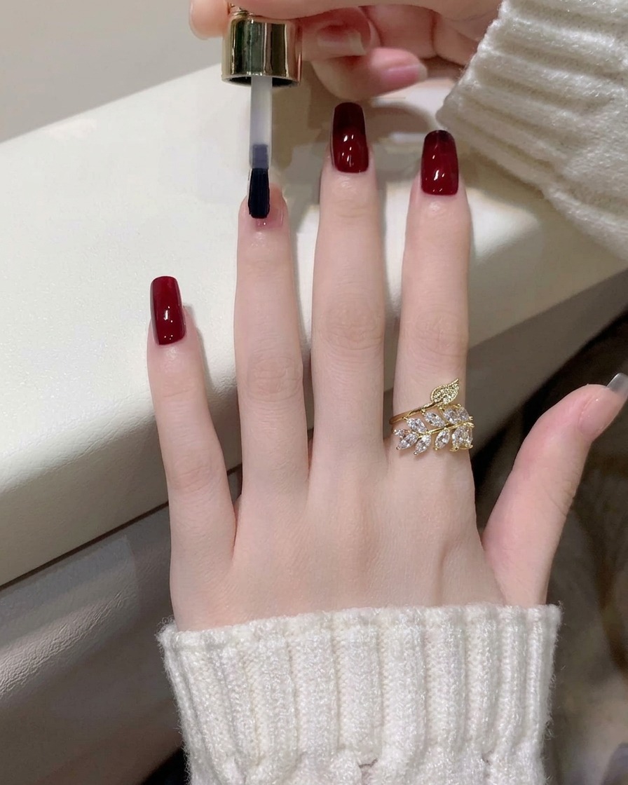 Primer plano de una segunda capa de esmalte de gel rojo vino siendo aplicada en el dedo índice.