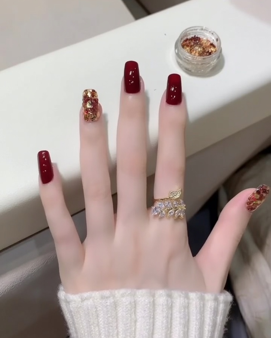 Primer plano de un pincel aplicando un top coat transparente y brillante sobre uñas rojas y la uña con brillo.
