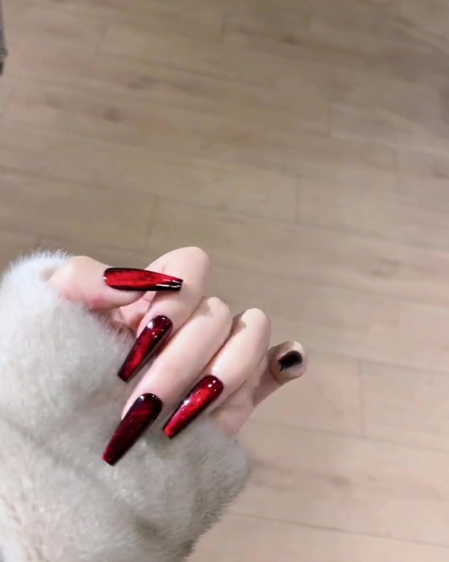 Un imán colocado sobre una uña cubierta con gel magnético rojo húmedo para dar forma a las partículas brillantes en una línea.