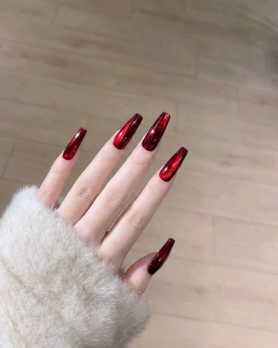 Un pincel aplicando una capa suave y transparente de top coat brillante sobre la uña de ojo de gato roja curada.