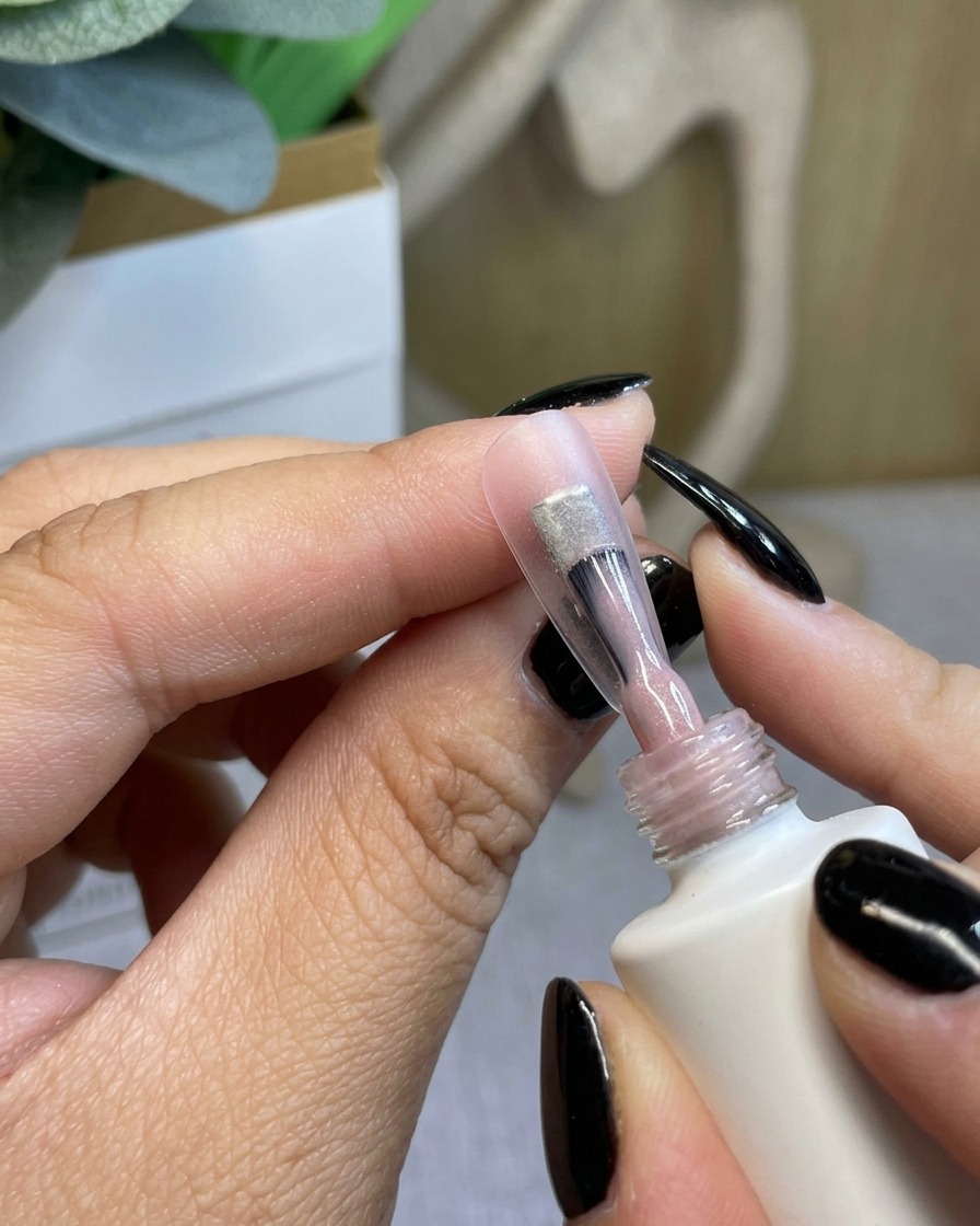 Un pincel aplicando una capa base de gel transparente y ligera sobre una uña natural.